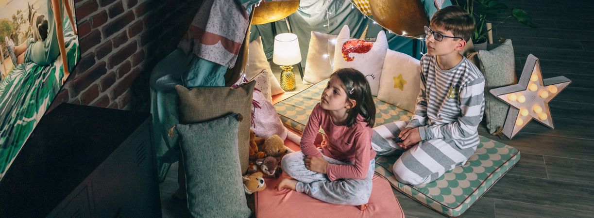 Banner of boy and girl looking tv show sitting on living room at night. Domestic life concept.