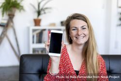 Woman showing a screen of a smart phone sitting on a sofa 4MGKel