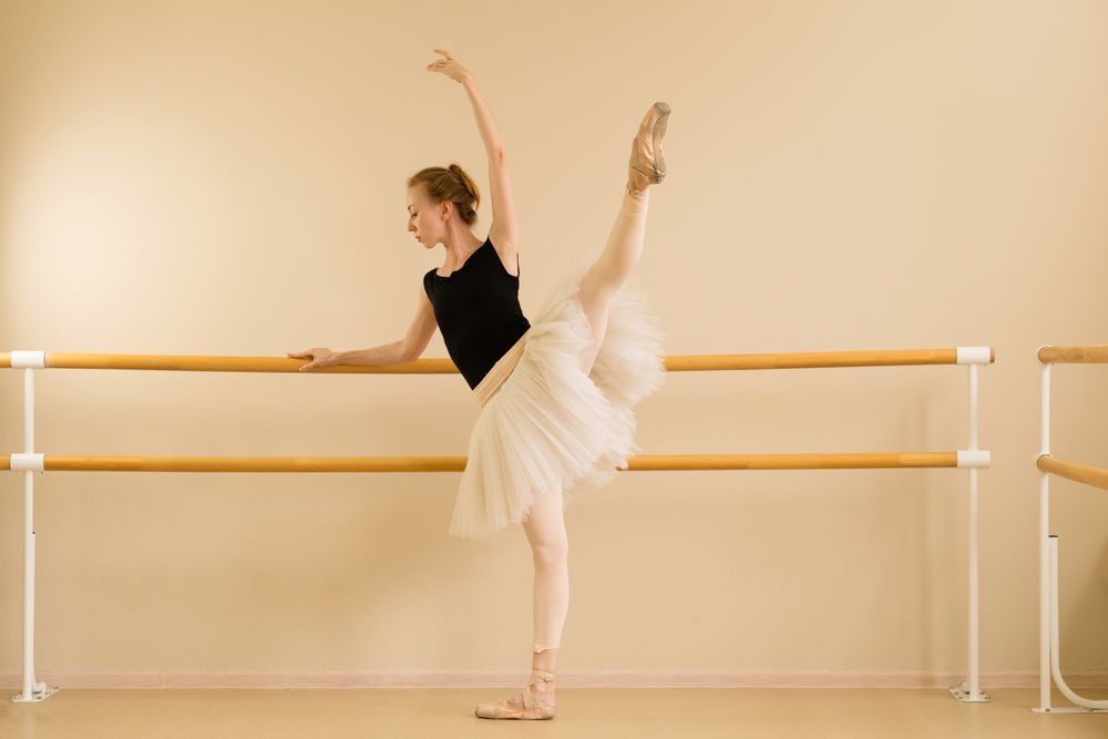 Ballet dancer holding pointe shoe in high leg extension