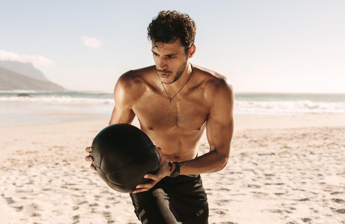 Fit male using weighted ball to do ab exercises on a beach