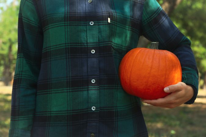 Woman in checkered shirt hold pumpkin outdoor