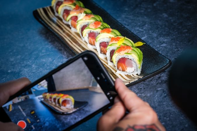 Unrecognizable person taking photo of sushi rolls on tray with smartphone