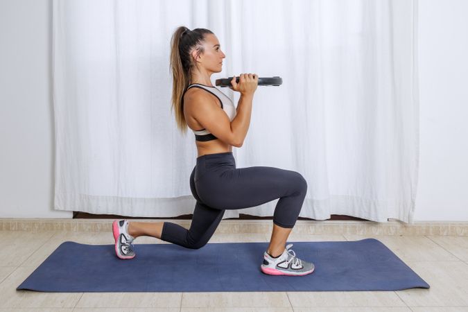Side view of woman doing leg and arms workout with barbell