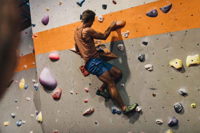 Athletic male climbing rock wall at fitness gym