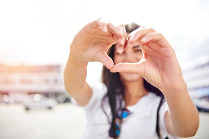 Woman’s face obscured by heart shape she’s making with her hands