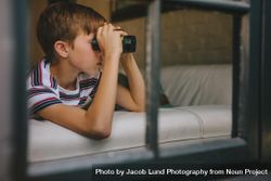 Curious boy looking out the window with binocular 0LQwe5