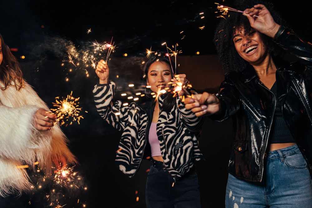 Three female friends smiling with sparklers at a party