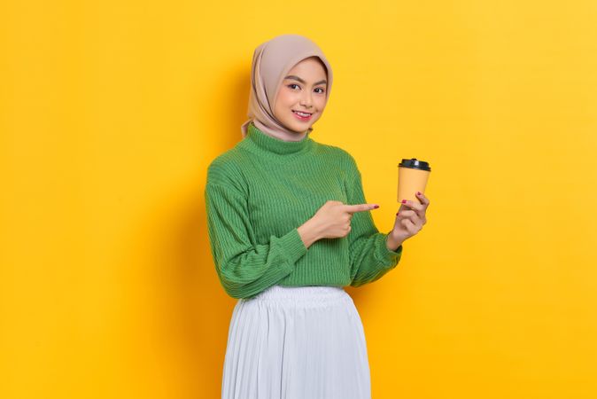 Smiling woman in headscarf pointing to to go coffee cup