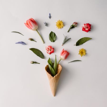 Ice cream cone with colorful flowers on light  background