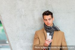 Young man wearing winter coat looking at phone screen against cement pillar 5r9DB7
