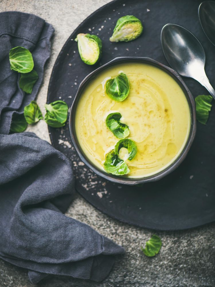 Bowl of Brussels sprout soup, on dark plate, garnished with fresh sprouts, vertical composition