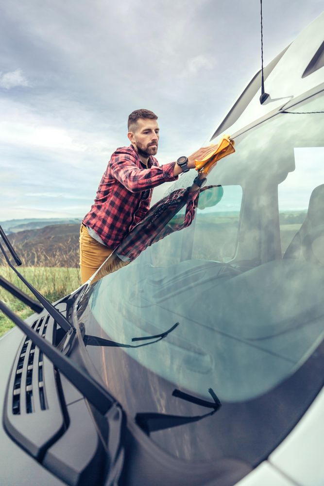 Man in checkered red shirt cleaning van’s front window with windshield wiper’s up, vertical