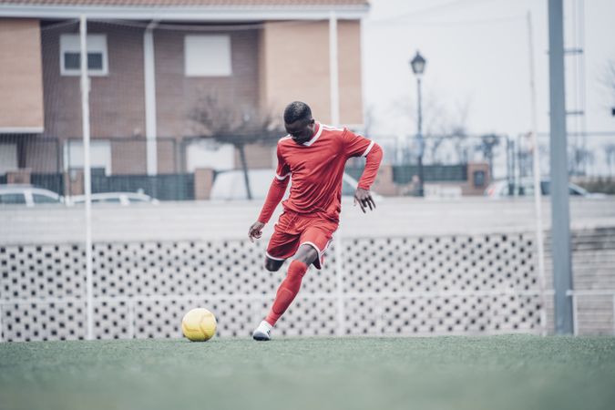 Black soccer player with red outfit playing soccer.