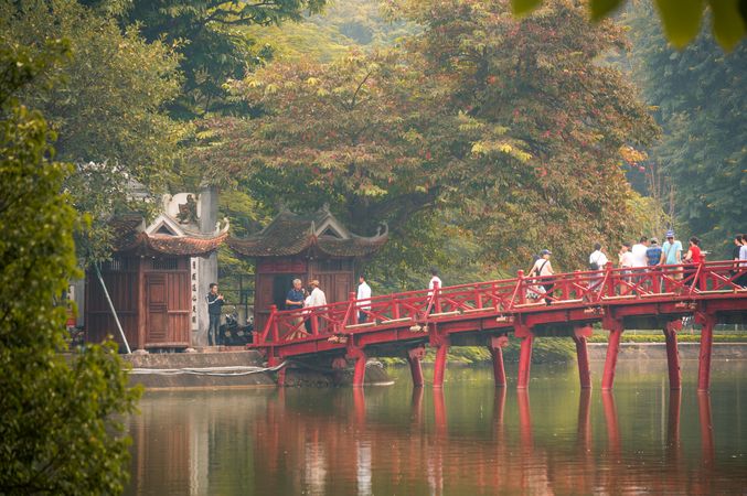 Group of people walking on red bridge near temple in Vietnam