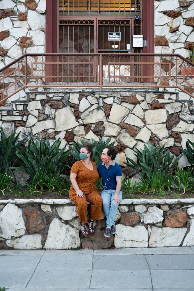 Cute married couple sitting on rock wall near sidewalk looking at their neighborhood