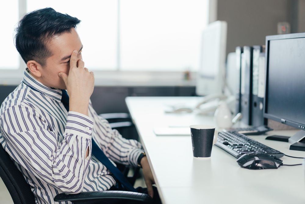 Frustrated Asian male employee sitting at desk in the office
