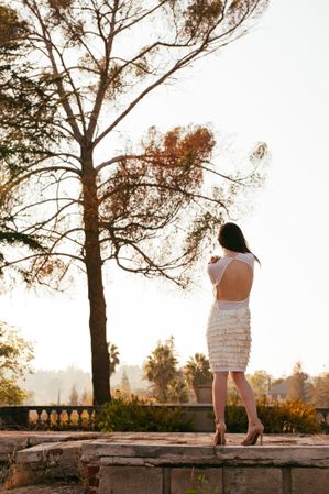 Back view of woman in white dress with open back standing on masonry foundation looking at view