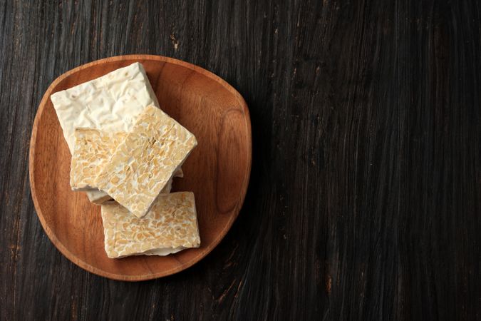 Top view slices of fresh tempeh on wooden plate with copy space