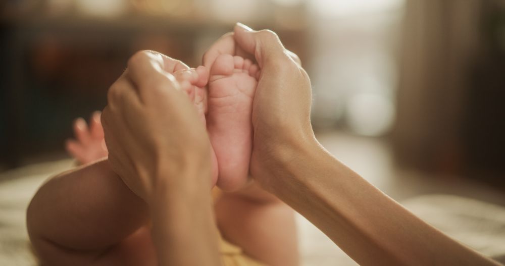 Close up on the Hands of an Affectionate Mother Forming a Heart Around the Little Feet of her Baby.