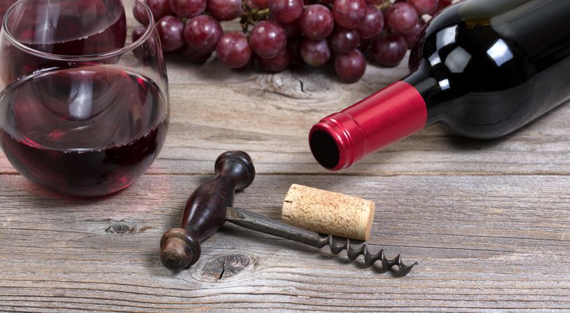 Vintage corkscrew with red wine bottle with grapes and drinking glasses in background