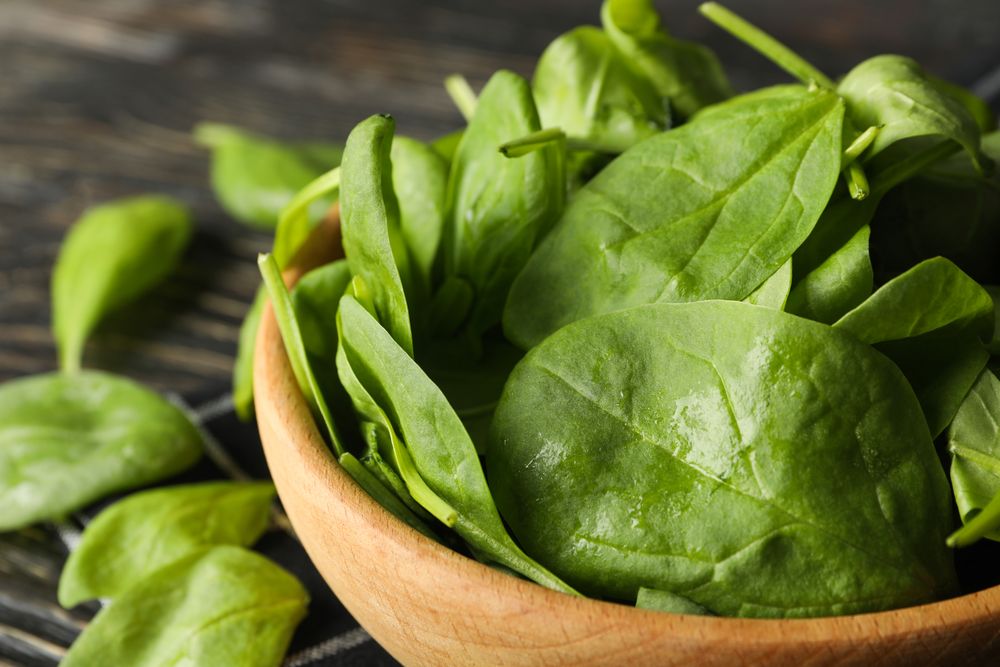 Wooden bowl with spinach and napkin on wooden background