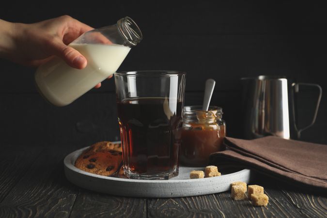 Woman pours a milk in glass of coffee. Composition with ice coffee