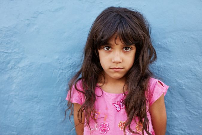 Close up portrait of  little girl standing against blue wall