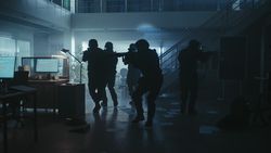Masked Team of Armed SWAT Police Officers Move in a Hall of a Dark Seized Office Building with Desks and Computers.
