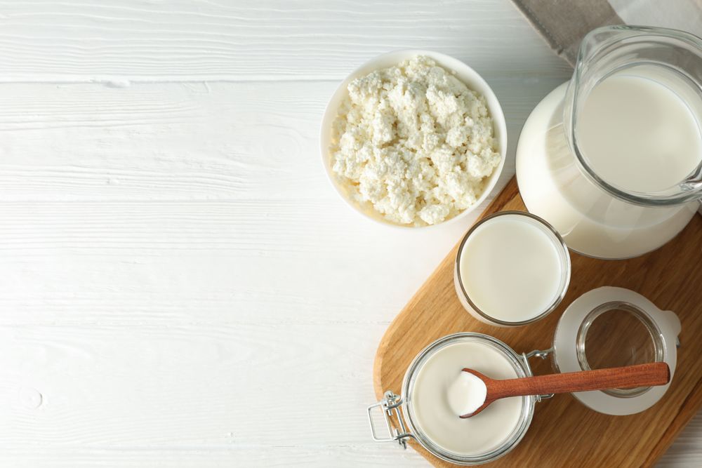 Flat lay. Fresh dairy products, board and towel on plain wooden table