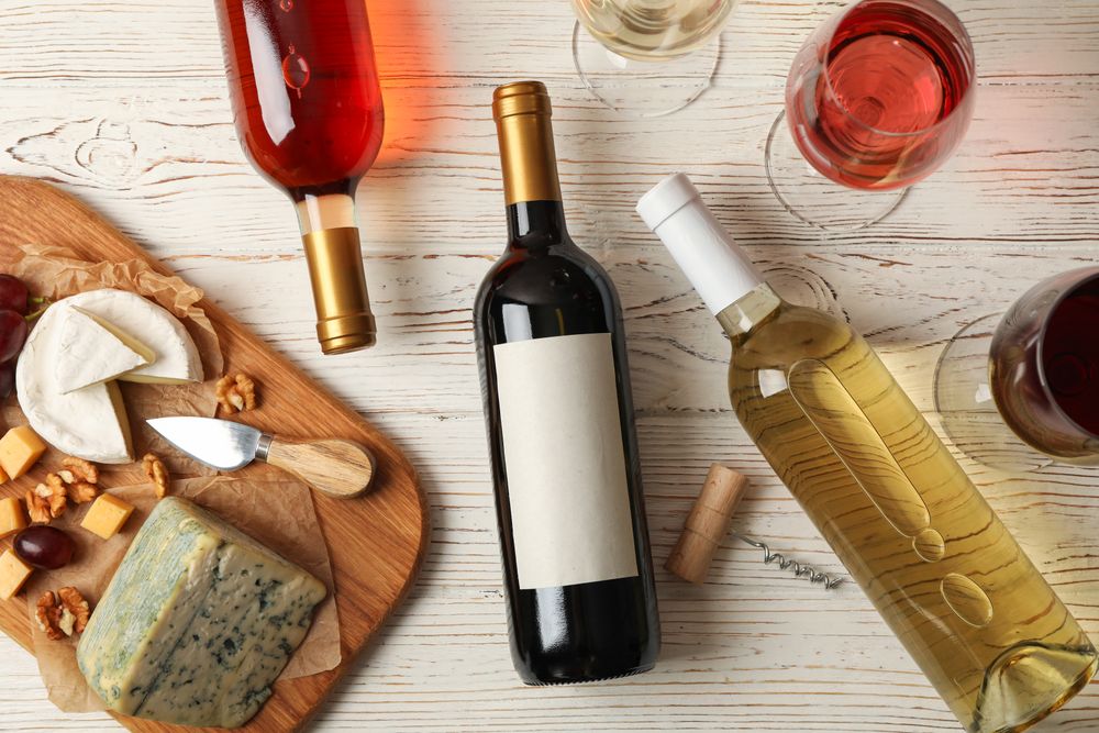 Grape, cheese, bottles and glasses with different wine on light wooden background, top view