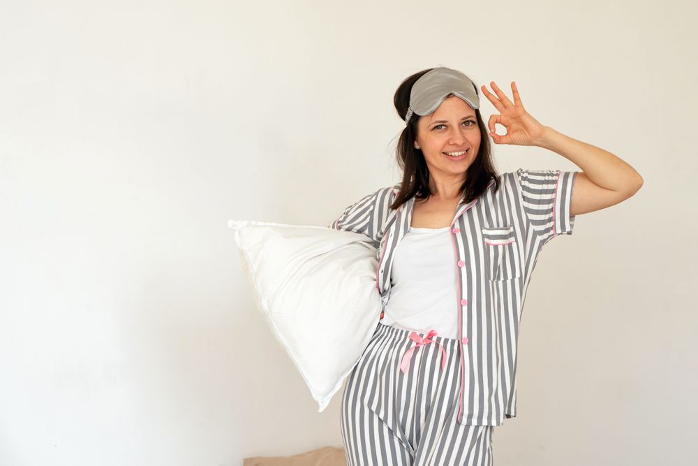 Woman making OK sign with hand, holding pillow in bed.