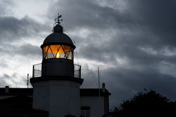 Shining lighthouse against cloudy sky