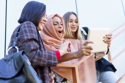 Three happy women happily looking at something on digital tablet