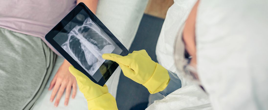 Doctor in protective suit examining x-ray of patient on tablet