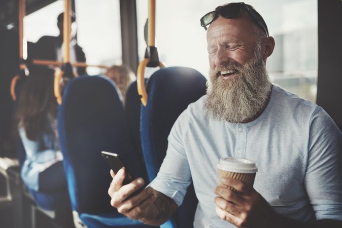 Man with gray beard smiling and video calling while on public transport