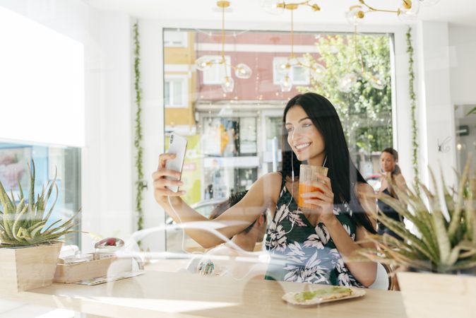Woman with healthy drink taking selfie in cafe