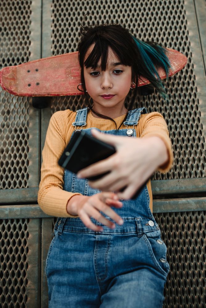Girl with smartphone and skateboard lying on walkway