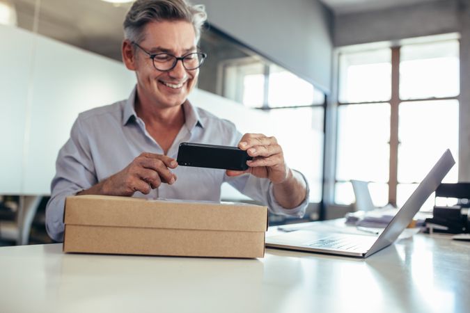 Smiling mid adult man taking scanning a delivery box on his desk