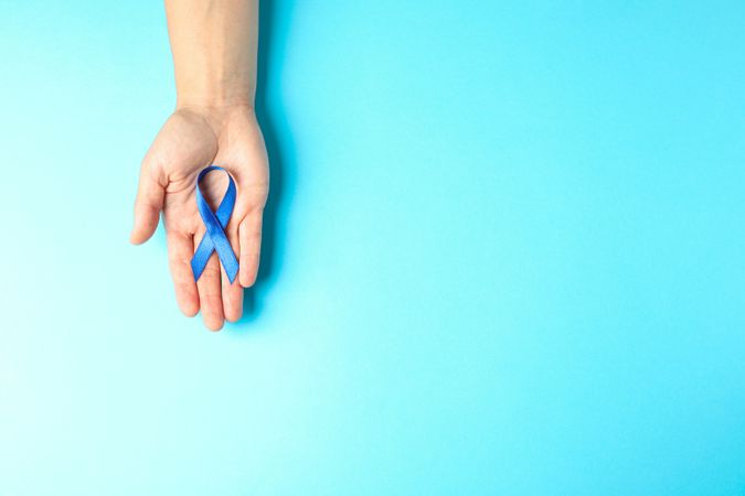 Female hand hold blue awareness ribbon on color background, space for text