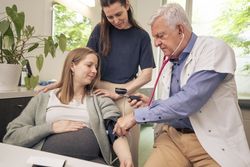 Doctor checking a pregnant woman's blood pressure in a clinic.