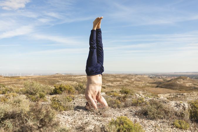 A gray-haired man performs a yoga headstand, during a yoga session in the countryside