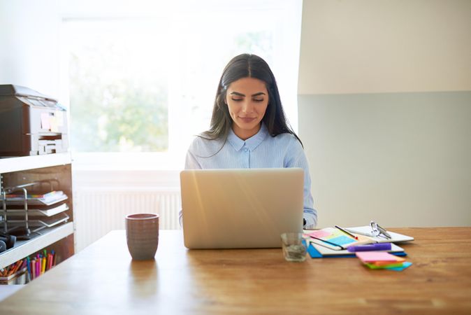 Confident woman in blue shirt working on her laptop in bright home office
