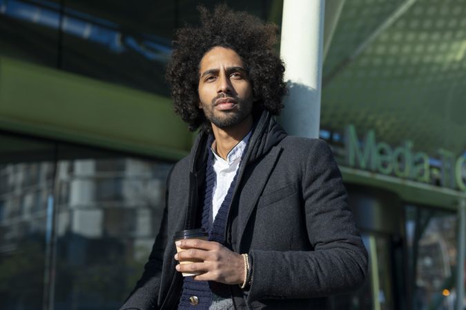 Portrait of Black man in jacket standing outside of building holding warm beverage