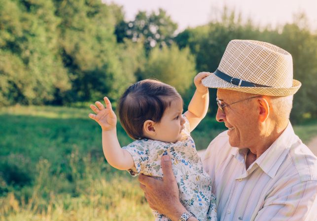 Baby girl playing with hat of older man outdoors