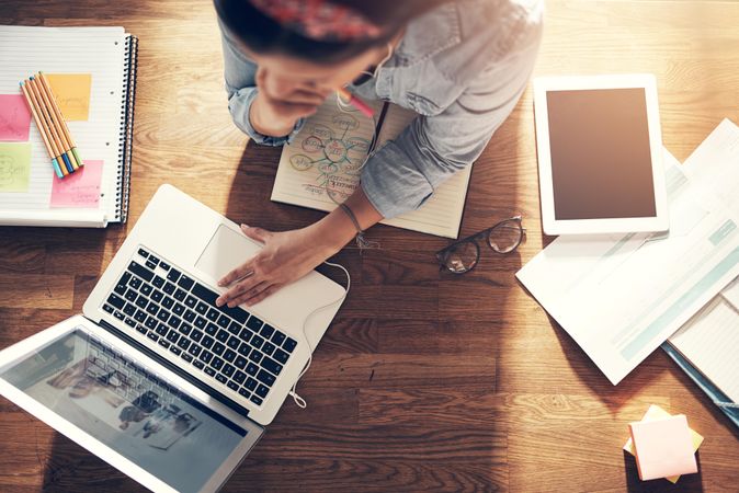 Top view of woman reading on laptop in home office with notebook