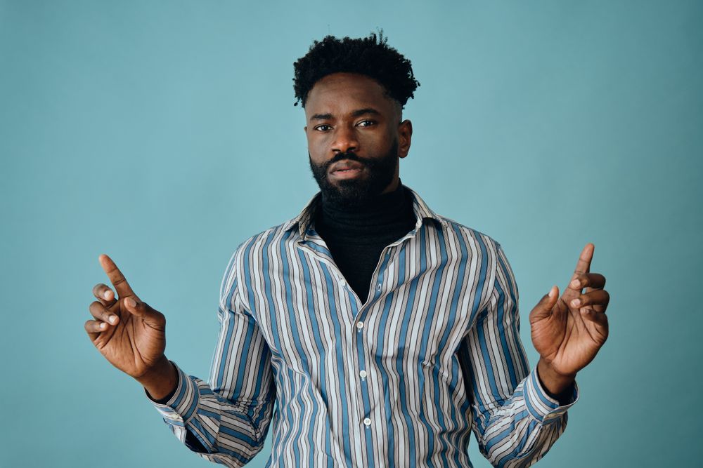 Serious Black man in striped shirt and jeans pointing up with both hands