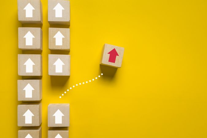 wooden blocks with up arrows and one different direction red arrow isolated on yellow background. leadership concept