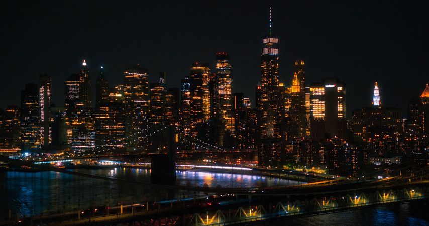 Iconic New York City Nightlife Landscape Over East River with Skyscrapers, Manhattan and Brooklyn Bridges, Cars and Ferry Boats. Cinematic Night Urban Skyline with Office Buildings with Lights