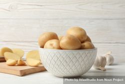 Side view of bowl full of potatoes on kitchen counter with garlic and cutting board, copy space 5QjOm4