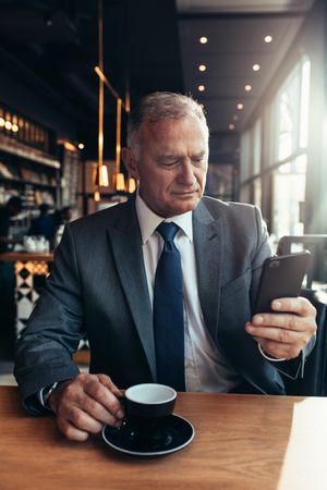 Older male wearing a suit looking at smartphone in cafe